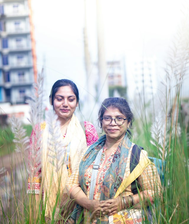 Two women standing in tall grass with apartment towers behind